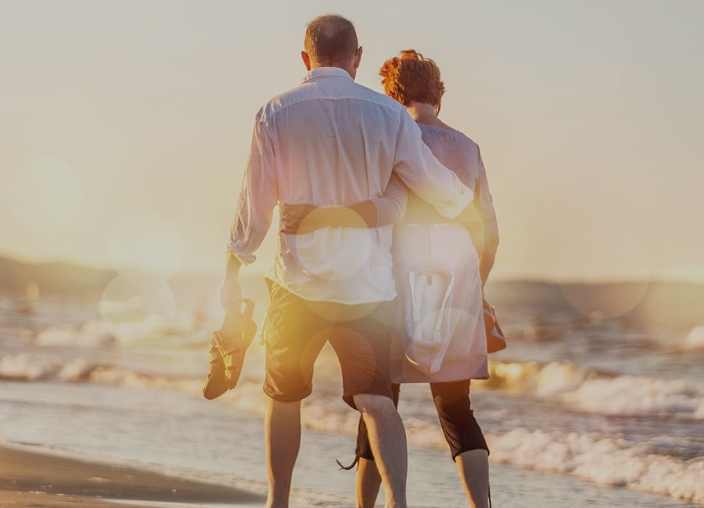 older couple walking on the beach barefoot