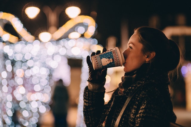 Woman sipping hot drink outside looking at Christmas lights