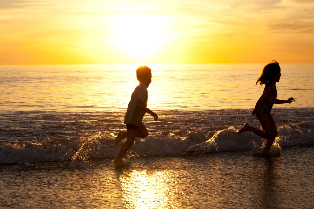 Two kids running in the white wash of the beach