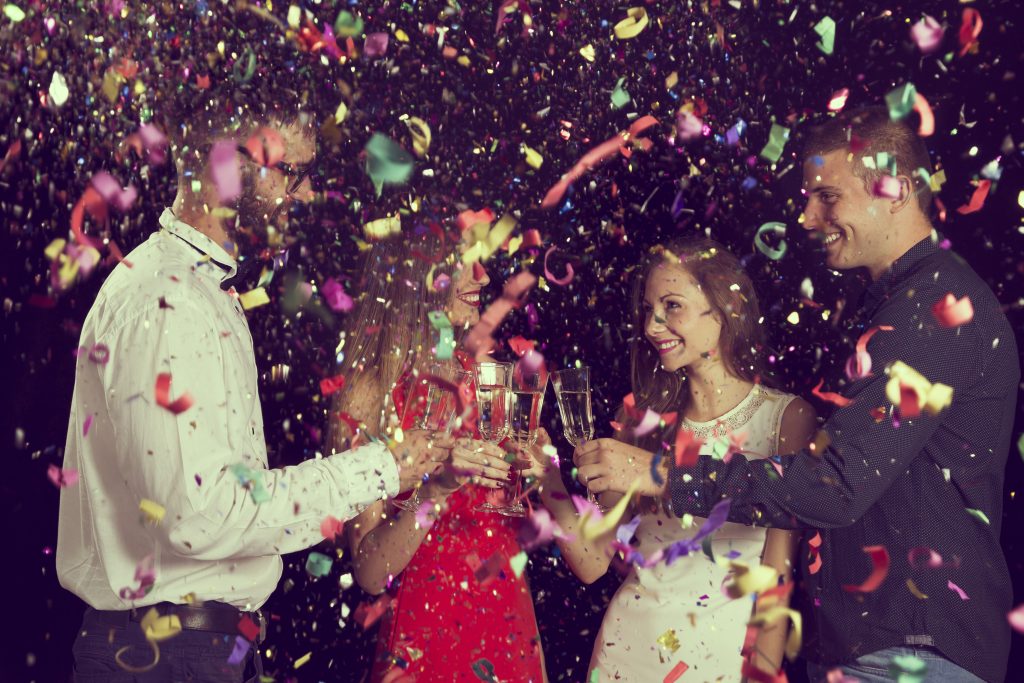 a picture of four young people making a new years eve toast with champagne and confetti.